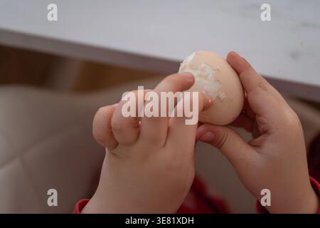 Aus der Nähe von Kinderhänden, die zu Hause ein gekochtes Ei schälen. Konzept von gesundem Snack, proteinreichen Lebensmitteln und täglichen Essgewohnheiten. Geeignet für Themen l Stockfoto