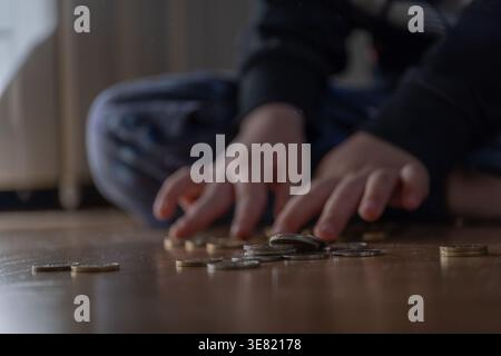 Nahaufnahme von Kinderhänden, die Münzen auf dem Boden in weichem Tageslicht zählen. Konzentrieren Sie sich auf frühzeitige Finanzerziehung, Spargewohnheiten und Geldbewusstsein. Ideal für Stockfoto