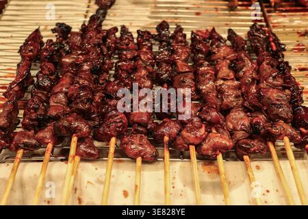 Gegrillte Hähnchenherzenspieße mit glänzender karamelisierter Textur auf dem thailändischen Nachtmarkt, authentischem Streetfood und exotischem Protein-Konzept. Stockfoto