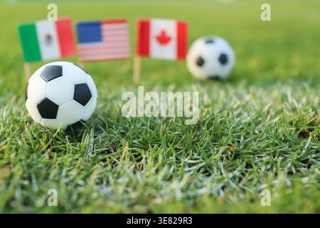 Fußball auf Rasen mit verschwommenen Fahnen der USA Mexiko Kanada symbolisieren globale Einheit und Konkurrenz Stockfoto