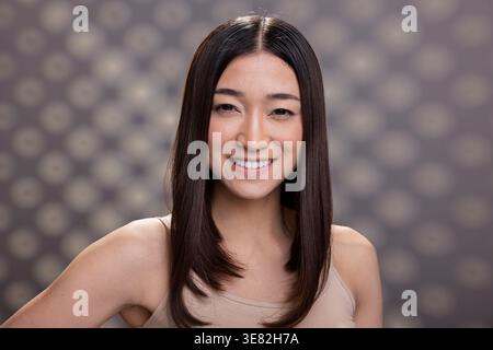 Porträt einer positiven asiatischen Frau mit offenem Lächeln und weichem Teint. Schöne Darstellung weiblicher Empowerment, Hautpflege und Selbstliebe, perfekt für moderne Wellness-Werbung. Stockfoto