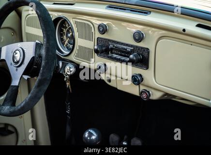 Oldtimer-Innenraum mit cremefarbenem Armaturenbrett und schwarzem Lenkrad. Das klassische Radio und die Knöpfe sitzen über einer Gangschaltung. Stockfoto