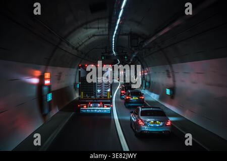 Fahrzeuge navigieren durch einen Flusstunnel, der von zyanblauen LED-Streifenlichtern beleuchtet wird, wobei rote Rücklichter in der Dunkelheit sichtbar sind. Motion Blur, London, Großbritannien Stockfoto