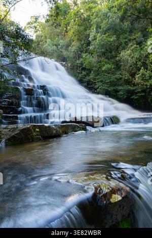 Der Wasserfall stürzt über geschichtete Felsen inmitten üppig grüner Wälder und sorgt für eine ruhige, unberührte nat-Szene Stockfoto