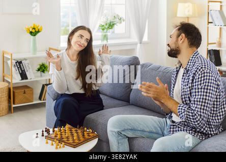 Paare teilen sich Schach zu Hause auf dem Sofa, verspielte Gesten und Lächeln zusammen Stockfoto