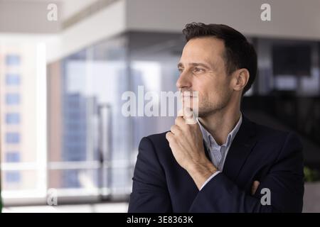 Porträt eines Geschäftsmannes mittleren Alters, der am Fenster steht und aus der Ferne blickt Stockfoto