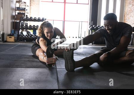 Verschiedene dunkle Sportbekleidung, die auf dem Boden des Fitnessstudios in der Nähe roter Fenster mit Hantelablage sitzt Stockfoto