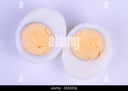 Zwei gekochte Eierhälften mit Eigelb, angeordnet auf weichem Lavendelhintergrund im Nahaufnahme-Food-Styling, glatte Eiweißtextur, bröckelig blassgelbes Eigelb, gelassen Stockfoto
