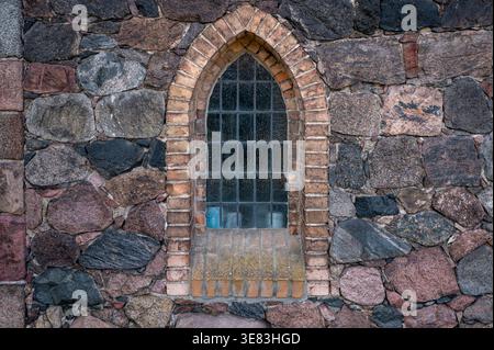 Historisches Spitzbogenfenster in einer Feldsteinmauer an der Kirche in Schwanebeck, Barnim, Deutschland. Der rötliche Ziegelrahmen ist kontrastreich. Stockfoto