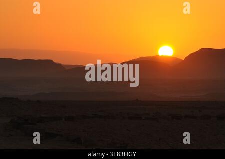 Während die Sonne hinter fernen Bergen untergeht, erfüllt der Himmel eine atemberaubende Auswahl an orangen und gelben Farben. Diese atemberaubende Aussicht fängt die ruhige Schönheit ein Stockfoto