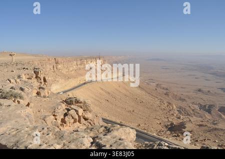 Eine wunderschöne gewundene Straße schlängelt sich durch eine trockene Wüstenlandschaft. Die felsigen Klippen erheben sich scharf, und der Horizont erstreckt sich endlos unter einem klaren Himmel Stockfoto