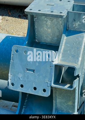 Metallteile sind in einem Baubereich angeordnet. Verschiedene Formen und Bohrungen sind sichtbar. Stahlprofile werden auf dem Boden platziert. Sonnenlicht scheint auf t Stockfoto