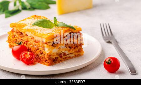 Traditionelle Lasagne mit Bolognesesauce, belegt mit Basilikumblättern, serviert auf einem weißen Teller Stockfoto