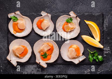 Rohe Jakobsmuscheln mit ZitronenPetersilie auf einem schwarzen Steinteller Stockfoto