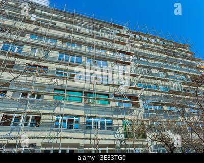 Arbeiter sind in einem großen Gebäude mit Gerüsten beschäftigt. Die Gebäudefassade wird repariert oder lackiert. Die Szene zeigt viele verwendete Werkzeuge und Materialien Stockfoto