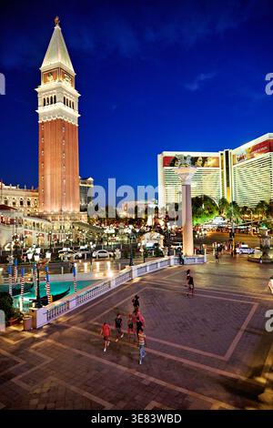 Die Leute laufen in der Nähe des Venetian Hotels, während die Dämmerung sich in Las Vegas niederlässt. Die Lichter beginnen auf den Gebäuden zu leuchten. Stockfoto