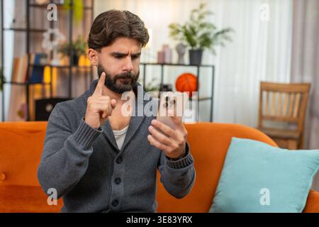 Indischer Mann zu Hause spielt Handy-Casino verliert Wette Seufzer hält Kopf reibt Stirn, keine Geste. Arabianer auf dem Sofa sieht Ergebnis traurig sagt nein mit Hand bestürzt Stimmung nach dem Verlust des Online-Glücksspiels Stockfoto