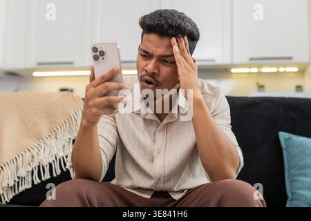 Der indische Mann zu Hause spielt die mobile Spielrunde verliert die Facepalm verärgert und ist bereit für das Rückspiel. Arabian Guy auf Sofa Tips versuchen Sie es erneut auf Smartphone Pläne Comeback konzentriert sich auf die nächste Stufe und die Wiederherstellung der Punktzahl Stockfoto