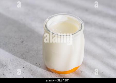 Cremiger Joghurt in einem kleinen Glas mit einer Schicht Fruchtpüree am Boden auf einer hellen Oberfläche. Stockfoto