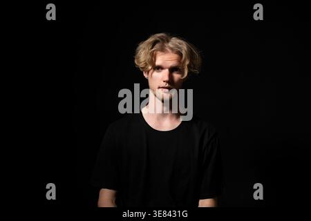 Verwirrter blonder Mann in einem schwarzen T-Shirt, der über ein Problem nachdenkt. Suche nach Antworten. Ein herausforderndes Gespräch führen. Zweifel empfinden Stockfoto