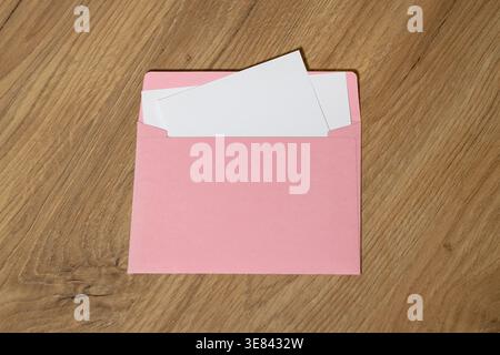 Ein rosafarbener Umschlag mit zwei weißen Buchstaben wird auf einem Holztisch mit natürlichem Holzmaserung platziert und schafft eine warme und einladende Szene Stockfoto