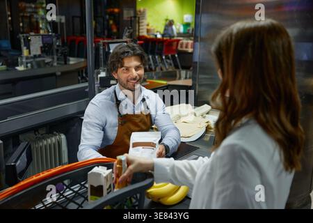 Ein Kassierer auf einer Schürze spricht mit einer Frau im Supermarkt an der Kasse Stockfoto