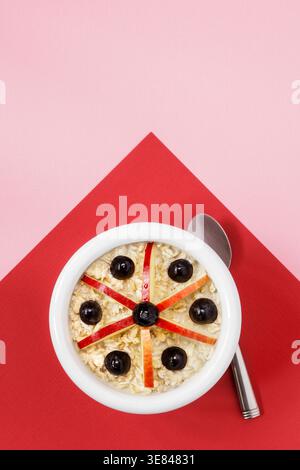 Weiße Schüssel mit Haferflocken, Äpfeln und Trauben auf rotem und rosa Hintergrund Stockfoto
