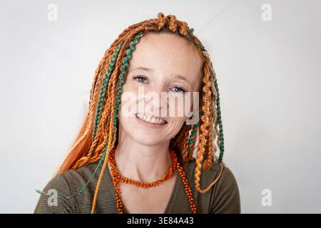 Nahaufnahme Porträt einer lächelnden Frau mit Ingwer Dreadlocks, die in die Kamera schauen. Grauer Hintergrund Stockfoto