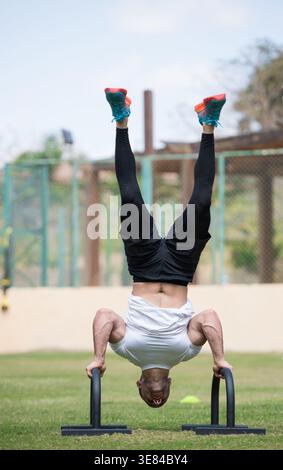 Arabischer Mann aus dem Nahen Osten, der während des CrossFit-Workouts im Outdoor-Fitness-Park einen Handstand-Liegestütze durchführt Stockfoto