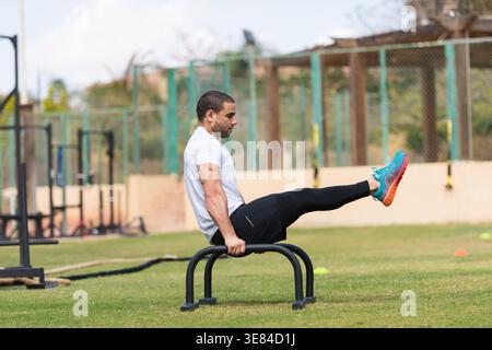 Sportlicher Mann, der beim CrossFit Workout im Freien L-Sit auf parallelen Bars durchführt Stockfoto