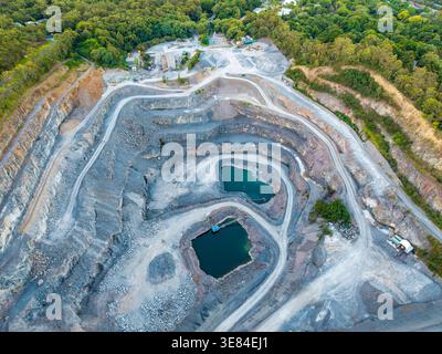 Ein Drohnenfoto zeigt einen großen Steinbruch im Tagebau und zeigt Terrassenmauern, zwei überflutete Gruben und betriebliche Maschinen, umringt von Stockfoto