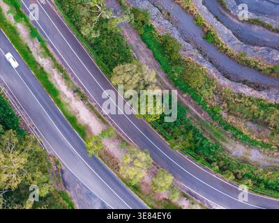 Ein Blick von oben zeigt eine mehrspurige Straße, die sich durch üppige Vegetation und entlang eines gemeißelten Felsendamms in Brisbane schlängelt. Stockfoto