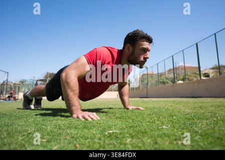 Mann, der Liegestütze im Freien in einem CrossFit-Fitness-Studio mit fokussiertem Ausdruck macht Stockfoto