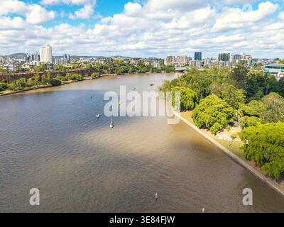 Der Brisbane River fließt vorbei an urbanen Hochhäusern und grünen Parklandschaften, die ein auffälliges zweifarbiges Wasserphänomen mit mehreren Segelbooten bieten. Stockfoto