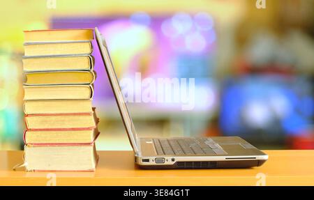 Laptop-Computer und Stapel Bücher, verschwommenes Büro im Hintergrund. Schlagen Sie die Uhr, Büroarbeit, Forschung, Bildungskonzept. Kostenloser Kopierraum. Stockfoto
