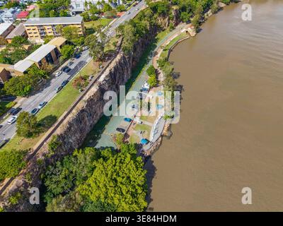 Aus der Vogelperspektive auf den Brisbane River, die städtische Parkanlage und eine Straße mit Autos, die sich an felsigen Klippen in Brisbane, Australien, schmiegt. Stockfoto