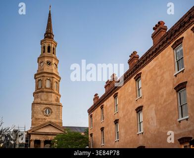 Charleston, SC - USA - 27. März 2026 die St. Philip's Church im historischen Charleston, SC, erhebt sich mit ihrem berühmten Turm neben einem alten pfirsichfarbenen Gebäude u Stockfoto