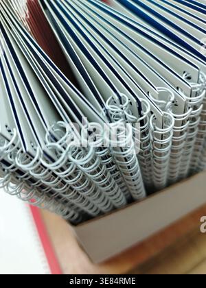 Stapel spiralgebundener Notizbücher mit weißen Umschlägen und bunten Kanten, die ordentlich in einem Karton auf einer Holzoberfläche angeordnet sind Stockfoto