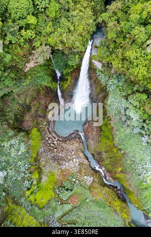 Blick aus der Vogelperspektive auf den üppigen tropischen Regenwald mit türkisfarbenen Stromschnellen und einer kleinen hölzernen Brücke über einen felsigen Bach. Stockfoto
