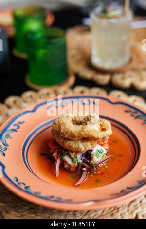 Gourmet-Vorspeise mit frittierten Meeresfrüchten, garniert mit geschnittenen Zwiebeln und Kräutern in Tomatensauce auf dekorativem Teller, geringe Tiefe des Feldes, gemütliches Restaurant setti Stockfoto