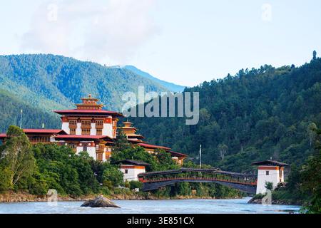 Traditionelles bhutanisches Dzong-Kloster mit gestuften roten Dächern auf einem bewaldeten Hügel vor nebeligen Bergen, heiterer buddhistischer Architektur und Natur-la Stockfoto