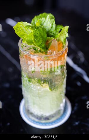 Nahaufnahme eines erfrischenden Cocktails im Mojito-Stil mit Minzgarnitur und Eis in einem strukturierten Highball-Glas auf dunklem Hintergrund. Stockfoto