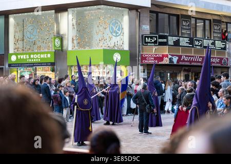 Almeria, Spanien - 30. März 2026: Peinfarbige Pönitenten stehen während einer Karwochenprozession in Bildung, während die Zuschauer die Straße in der Stadt cen säumen Stockfoto