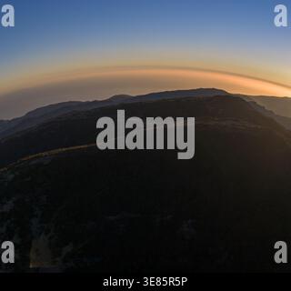 Aus der Vogelperspektive auf Madeira Bergrücken mit terrassenförmig angelegten Hängen und schwachen Bergpfaden, mehrschichtigen Silhouetten und einem warmen Dunstbogen bei Sonnenuntergang unter tiefen Windungen Stockfoto