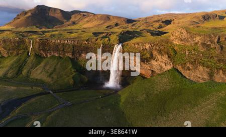 Der majestätische Seljalandsfoss-Wasserfall, der über zerklüftete Klippen fällt, mit seinem weißen Wasser im Kontrast zur grünen Landschaft von Stockfoto