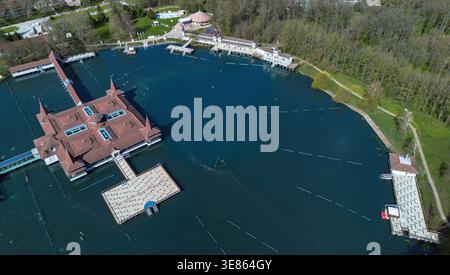 Blick aus der Vogelperspektive auf den Hévíz-See, wo das dunkelblaue Wasser auf die warmen Farbtöne der Badehausdächer und das umliegende üppige Grün trifft, Hévíz, Zala, Hu Stockfoto