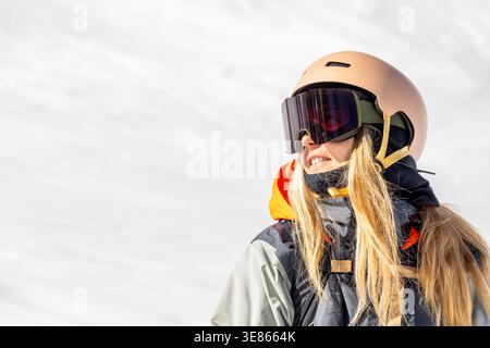 Porträt einer Snowboarderin mit Helm und Schutzbrille, lächelnd im hellen Winterlicht auf einer verschneiten Piste in den Pyrenäen, Outdoor-Sport Stockfoto