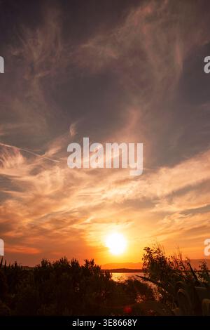 Ein atemberaubender Blick auf einen Sonnenuntergang über dem Meer, wo die warmen Farbtöne der Sonne den Himmel mit lebhaften Farben überstreichen und eine dramatische Szene mit Silhouetten schaffen Stockfoto