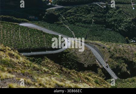 Aus der Vogelperspektive auf eine gewundene Bergstraße mit Autos, die durch üppige Terrassen und bewaldete Hänge auf La Palma auf den Kanarischen Inseln fahren und dramatische Kurven zeigen Stockfoto