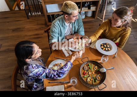 Blick von oben auf Freunde, die mediterrane Speisen in einem gemütlichen Restaurant teilen, Gläser anstoßen und einen entspannten Dining-Lifestyle mit Paella und Tapas genießen Stockfoto